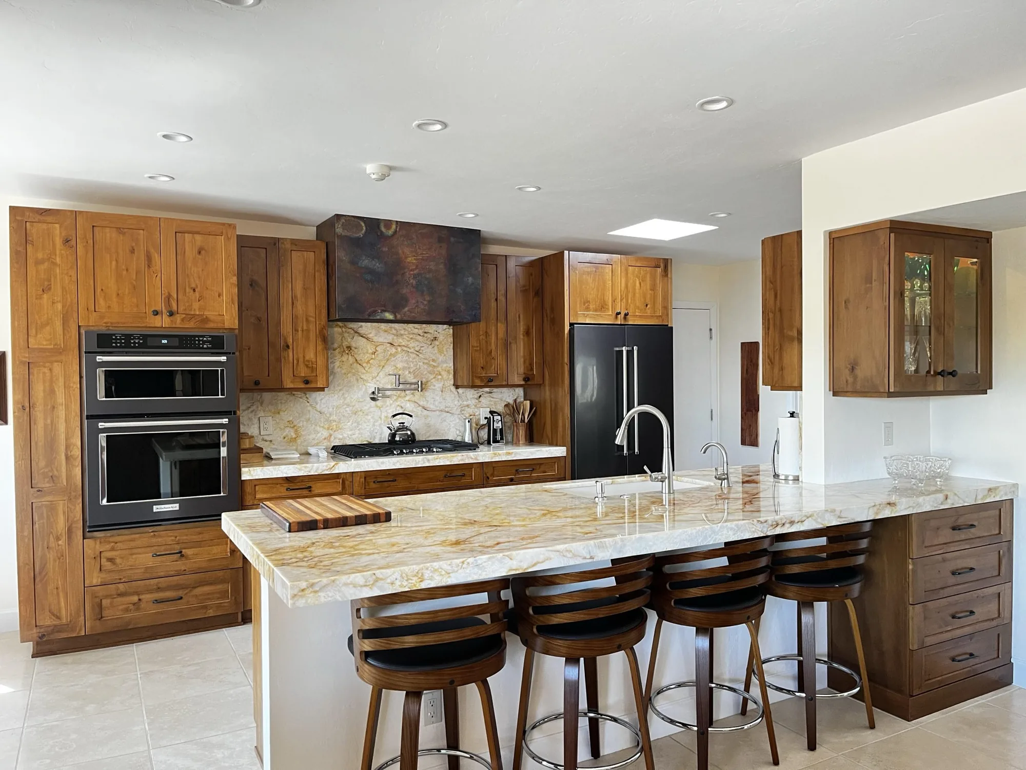 Knotty alder kitchen with a copper hood and a stone island, designed by Beyond Cabinets by Mueller