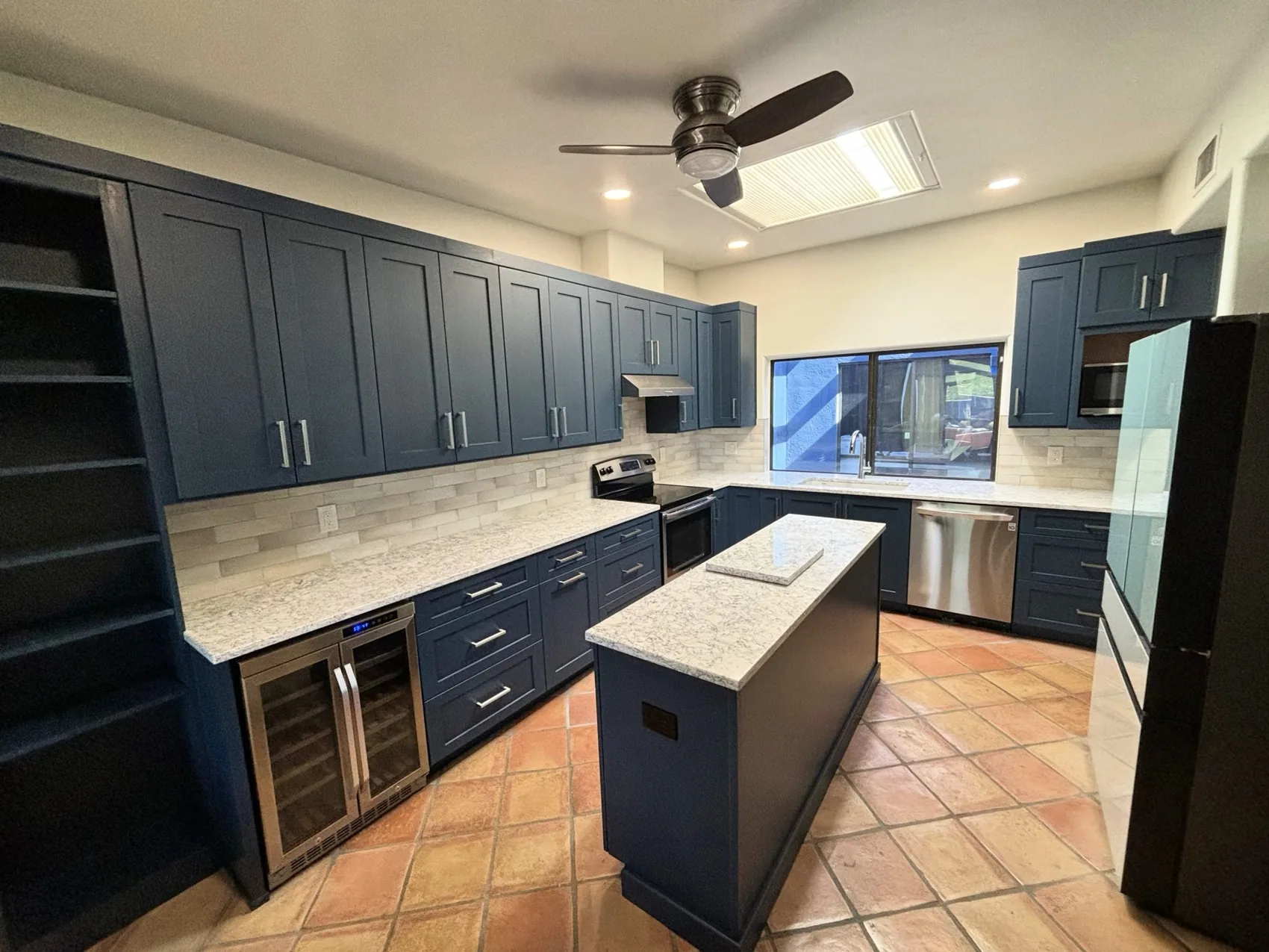 Navy kitchen cabinetry with a stone island over saltillo tile