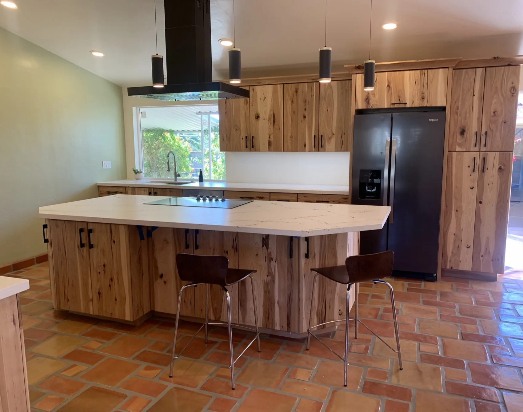 Hickory kitchen with an island and a black hood over terracotta tile
